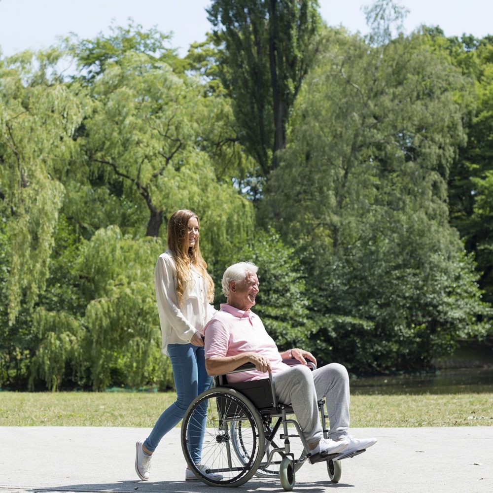 Young girl walking in the park with elder man on a wheelchair