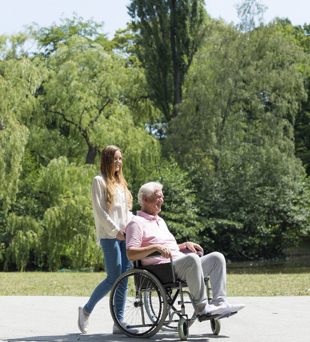 Young girl walking in the park with elder man on a wheelchair