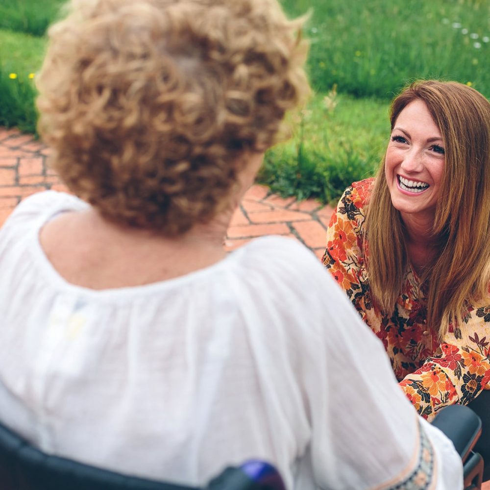 Happy young woman caring elderly woman in a wheelchair in the garden